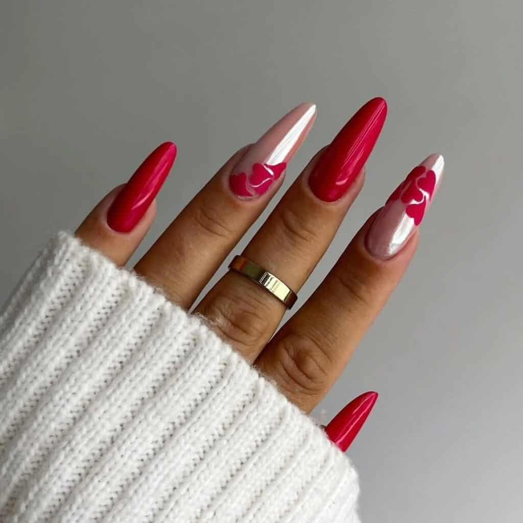 Hand with long almond shaped nails featuring glossy red polish and nude accent nails with red heart designs, creating a classic Valentine’s inspired February manicure.