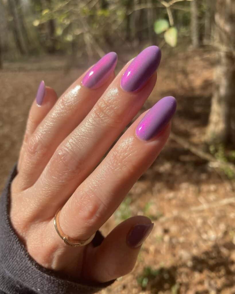 Hand with long almond shaped nails featuring glossy lavender and purple polish with a subtle shimmer, photographed outdoors in natural light for a soft spring inspired manicure.